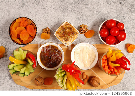 Middle East plate, Healthy food cuisine background with hummus bowl and raw vegetable sticks, nuts and dried apricots. Hummus platter with appetizers, traditional vegan snacks, oriental cuisine Middle East plate, Healthy food cuisine background with hummus bowl and raw vegetable sticks, nuts and dried apricots. Hummus platter with appetizers, traditional vegan snacks, oriental cuisine 124595908