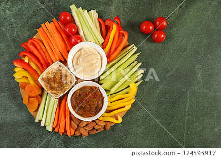 Hummus platter with appetizers, healthy food kitchen background with hummus bowl and raw vegetable sticks, nuts and dried apricots. Middle East plate, traditional vegan appetizers, oriental cuisine Hummus platter with appetizers, healthy food kitchen background with hummus bowl and raw vegetable sticks, nuts and dried apricots. Middle East plate, traditional vegan appetizers, oriental cuisine 124595917