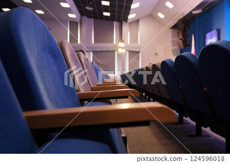 A conference room with rows of empty blue chairs and square lamps on the ceiling. With space to copy. High quality photo 124596018