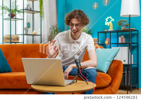 Happy blogger man recording podcast on couch, giving workshop speaking at microphone webinar at home 124596281