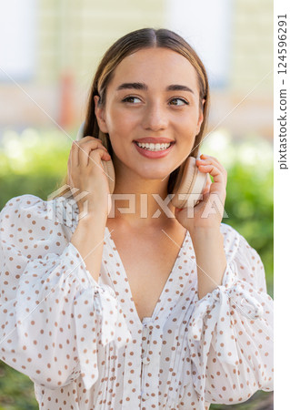 Happy young woman listening music taking off wireless headphones looking at side smiling outdoors 124596291