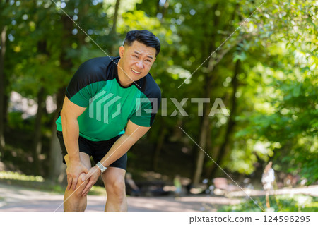 Chinese runner sportsman with muscle knee pain in park trauma injury while jogging leg muscle cramp 124596295