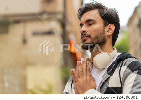 Religious Indian man praying with closed eyes to God asking for blessing while standing on street Religious Indian man praying with closed eyes to God asking for blessing while standing on street 124596301