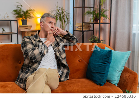 Thoughtful man rubbing chin looking aside with pensive expression pondering a solution at home room 124596330