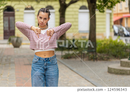 Displeased woman showing thumbs down sign gesture disapproval dissatisfied bad work on city street 124596343