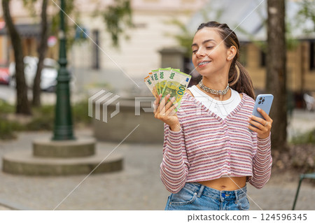 Happy woman counting money euro cash, use smartphone calculator app in urban city street 124596345