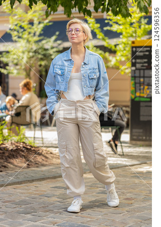Happy Caucasian young woman tourist traveler in glasses walking while looking around on city street Happy Caucasian young woman tourist traveler in glasses walking while looking around on city street 124596356