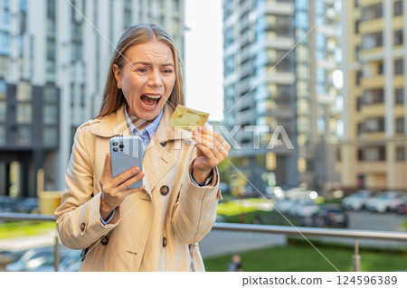Frustrated mature businesswoman girl using credit card and mobile phone on downtown city street Frustrated mature businesswoman girl using credit card and mobile phone on downtown city street 124596389