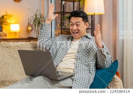 Excited man sitting on sofa using laptop receives good news victory celebrate lottery win at home Excited man sitting on sofa using laptop receives good news victory celebrate lottery win at home 124596414