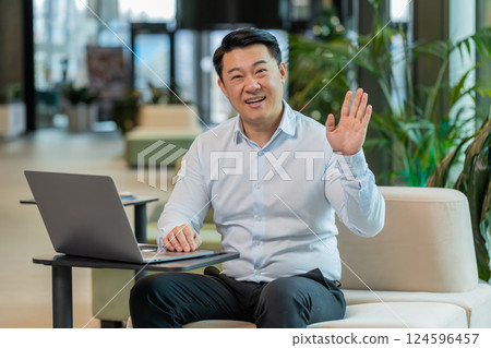 Happy middle-aged Chinese businessman looking at camera and waving hand hello in office lobby Happy middle-aged Chinese businessman looking at camera and waving hand hello in office lobby 124596457