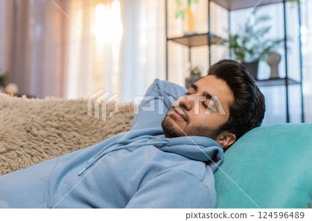 Tired Indian man lying on comfortable couch taking rest and daytime nap in living room at home 124596489
