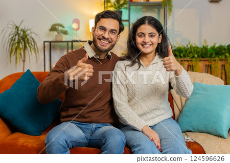 Smiling young Indian family couple man woman sitting showing thumbs up giving approval good feedback Smiling young Indian family couple man woman sitting showing thumbs up giving approval good feedback 124596626