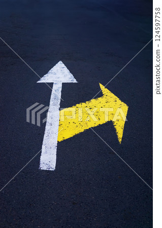 Two old directional arrows painted on asphalt show which way vehicles should turn at busy intersection in an urban area. Road marking with two directional arrows painted on dark asphalt 124597758