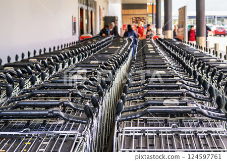 Many shopping carts stacked in rows outside supermarket entrance, ready for customer use. Shopping carts reflect consumerism, retail organization, urban shopping culture Many shopping carts stacked in rows outside supermarket entrance, ready for customer use. Shopping carts reflect consumerism, retail organization, urban shopping culture 124597761