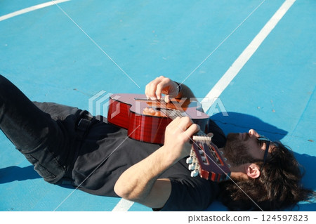 Man Lying On The Ground Plays Classical Guitar On Blue Floor Outdoor 124597823
