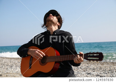 Kneeling Man Plays Guitar Musical Instrument On The Beach Near The Ocean Summer Kneeling Man Plays Guitar Musical Instrument On The Beach Near The Ocean Summer 124597830