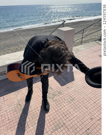 Street Artist Takes a Bow After Playing Classical Guitar on the Beach Near Ocean 124597836