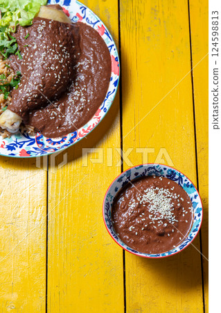 Delicious mole poblano served with tender chicken over a vibrant yellow table 124598813