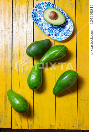 Fresh avocados arranged on a vibrant yellow wooden table with a decorative plate Fresh avocados arranged on a vibrant yellow wooden table with a decorative plate 124598815