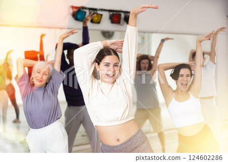 Happy young woman practising modern dance moves with other people in dance studio Happy young woman practising modern dance moves with other people in dance studio 124602286