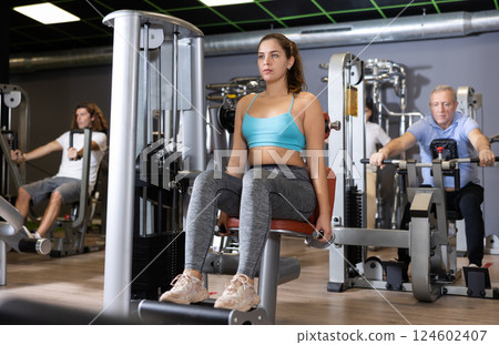 Young female training trains muscles of arms and press on simulator in gym 124602407