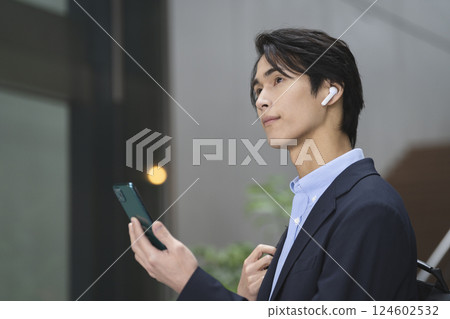一位年輕商人拿著智慧型手機,戴著耳機 一位年輕商人拿著智慧型手機,戴著耳機 124602532