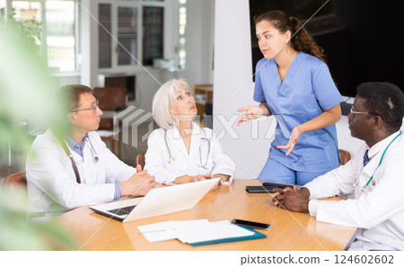 Young doctor talking to her colleagues sitting around table 124602602