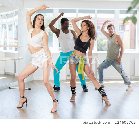 Female dancers at dance lesson in stiletto heels, in different choreographic poses, showing off their slim body in dance studio 124602702
