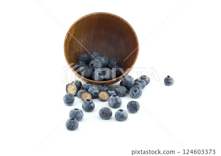 Wooden bowl spills blueberries onto a white surface, highlighting their freshness and natural appeal Wooden bowl spills blueberries onto a white surface, highlighting their freshness and natural appeal 124603373