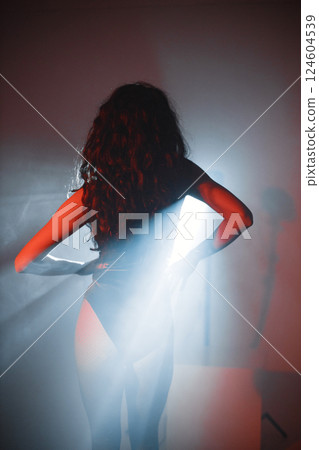 Young curly brunette girl posing for a photo. Girl wearing red velour bodysuit. Projectors light girl up. Young curly brunette girl posing for a photo. Girl wearing red velour bodysuit. Projectors light girl up. 124604539