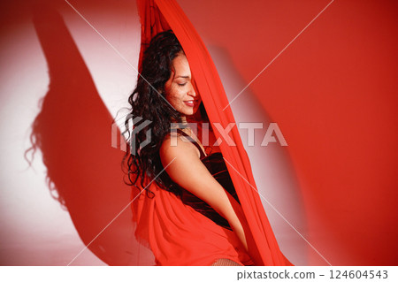 Curly brunette girl posing for a photo. Girl wearing velour bodysuit and is wrapped in red scarf. Projectors light girl up. 124604543