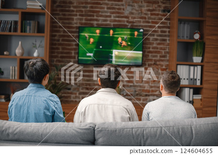Back view of male friends gathered at home to watch a football match. Men sitting on the couch in front of the big screen TV. Men actively support their favorite team and comment on the match 124604655
