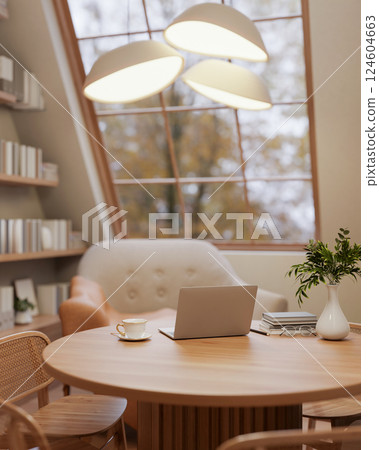 The wooden table and armchairs under the stylish lamp next to roof window in the earth tone room. The wooden table and armchairs under the stylish lamp next to roof window in the earth tone room. 124604663
