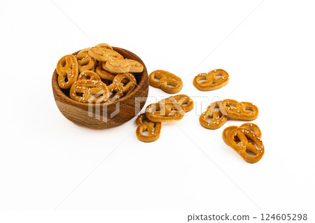 Crunchy pretzels served in a wooden bowl with some scattered on a white surface 124605298