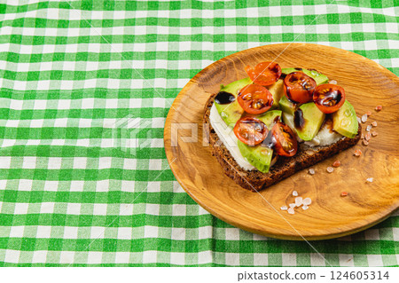 Avocado and tomato toast on a wood plate with a green checkered cloth Avocado and tomato toast on a wood plate with a green checkered cloth 124605314