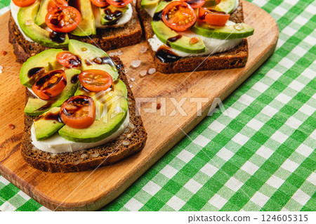 Fresh avocado and tomato toast served on wooden board with checkered background 124605315