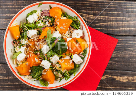 Fresh salad with persimmon, arugula, and feta cheese served on a wooden table 124605339