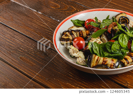Grilled eggplant and tomato salad with fresh basil on wooden table Grilled eggplant and tomato salad with fresh basil on wooden table 124605345