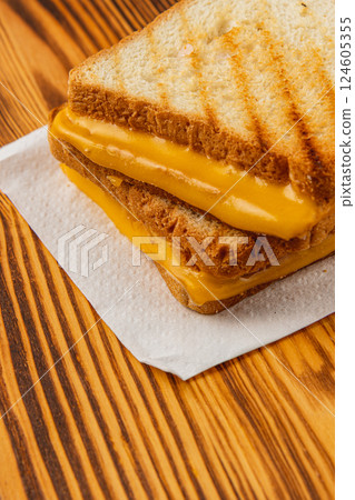Grilled cheese sandwich served on a white napkin atop a wooden table 124605355