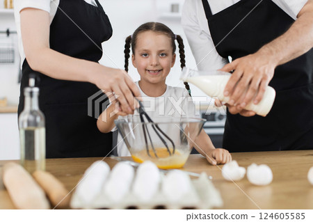 Caucasian family in kitchen preparing ingredients, young girl happily using whisk to mix. 124605585