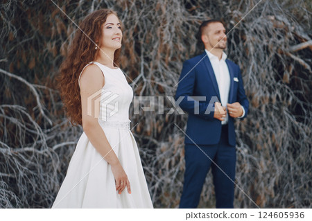 beautiful young long-haired bride in white dress with her young husband near gray branches 124605936