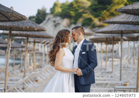 beautiful young long-haired bride in white dress with her young husband on the beach beautiful young long-haired bride in white dress with her young husband on the beach 124605973