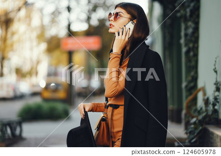styligh woman uses her cell phone as she walks through the city on a sunny warm day styligh woman uses her cell phone as she walks through the city on a sunny warm day 124605978