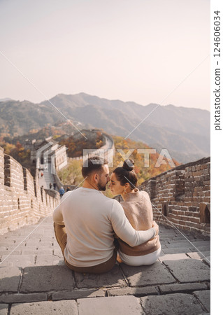 beautiful young couple sitting down and showing affection at the Great Wall of China. Newly married couple on their honemoon to Great Wall near Beijing China. Stylish couple exploring one of the beautiful young couple sitting down and showing affection at the Great Wall of China. Newly married couple on their honemoon to Great Wall near Beijing China. Stylish couple exploring one of the 124606034