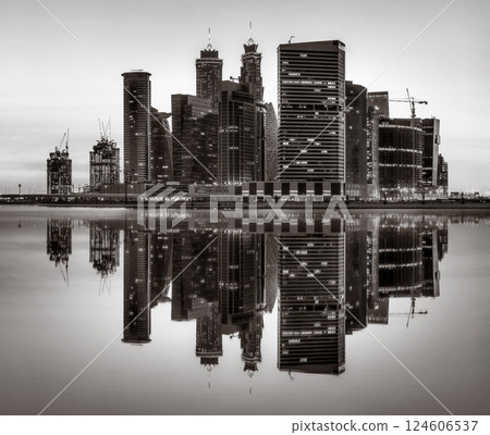 Monochrome city skyline with tall skyscrapers reflecting on calm water under a cloudy sky, Dubai Marina bay UAE Monochrome city skyline with tall skyscrapers reflecting on calm water under a cloudy sky, Dubai Marina bay UAE 124606537