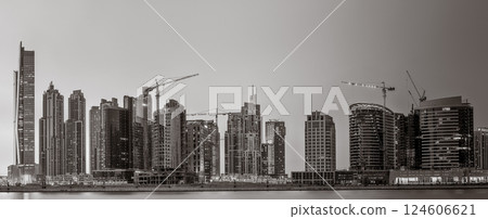 Monochrome city skyline with tall skyscrapers reflecting on calm water under a cloudy sky, Dubai Marina bay UAE Monochrome city skyline with tall skyscrapers reflecting on calm water under a cloudy sky, Dubai Marina bay UAE 124606621