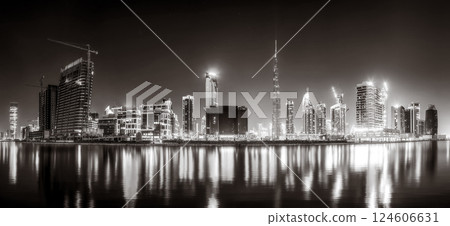 Urban city skyline with illuminated skyscrapers and waterfront railing in black and white at night, Dubai Marina bay UAE 124606631