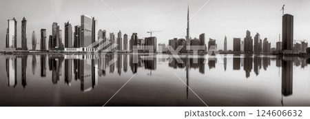 Monochrome city skyline with tall skyscrapers reflecting on calm water under a cloudy sky, Dubai Marina bay UAE 124606632