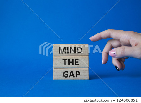 Mind the gap symbol. Concept words Mind the gap on wooden blocks. Beautiful blue background. Businessman hand. Business and Mind the gap concept. Copy space. Mind the gap symbol. Concept words Mind the gap on wooden blocks. Beautiful blue background. Businessman hand. Business and Mind the gap concept. Copy space. 124606851