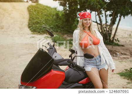 Attractive caucasian woman in a bikini swimsuit on a bike scooter near the beach in sunny weather. Attractive caucasian woman in a bikini swimsuit on a bike scooter near the beach in sunny weather. 124607091